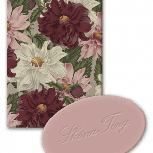 Tarjeta con estampado floral, con grandes flores rojas y blancas, acompañada de un objeto redondo de color rosa con texto en cursiva.