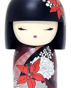 Una muñeca de madera con los ojos cerrados, cabello pintado de negro y patrones florales en rojo, blanco y negro sobre un vestido granate.