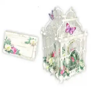 La JAULA DE FLORES BLANCA 3D006 es una decorativa jaula blanca adornada con flores y mariposas, que se presenta junto a una tarjeta floral a juego.