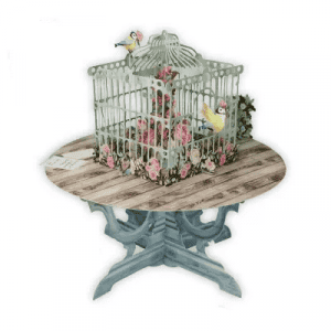 La JAULA DE PÁJAROS EN MESA 3D015 presenta una jaula decorativa con flores y pájaros sobre una mesa redonda de madera con pedestal.