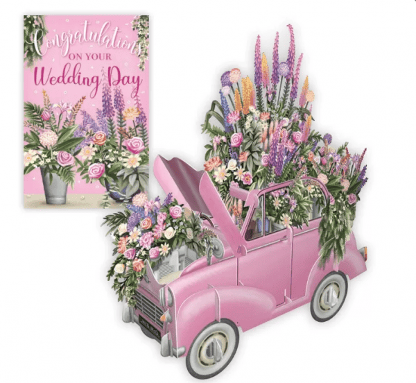 Un coche de boda 3D030 COCHE DE BODA ROSA-rosa lleno de flores de colores, emparejado con una tarjeta floral "Felicidades en el día de tu boda" de fondo.