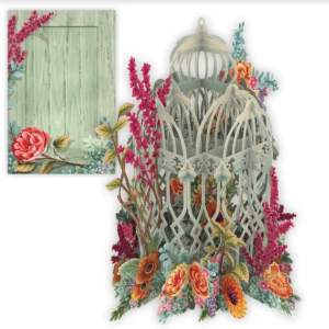 La 3D032 JAULA CON FLORES es una decorativa jaula de pájaros de papel en 3D rodeada de flores de colores, expuesta junto a una tarjeta verde con detalles florales en las esquinas.