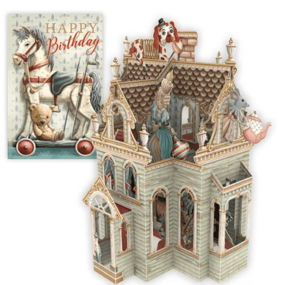 Tarjeta de cumpleaños vintage con un caballo balancín y un osito de peluche junto a una detallada casa de muñecas victoriana en miniatura con figuritas de animales y una mujer en su interior.