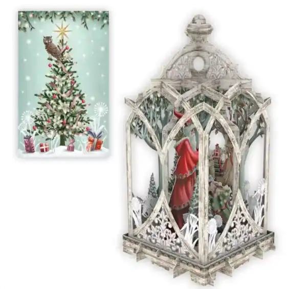Un farolillo de estilo vintage con una escena invernal y Papá Noel en su interior se sitúa junto a un árbol de Navidad ilustrado con regalos y un búho en la parte superior.